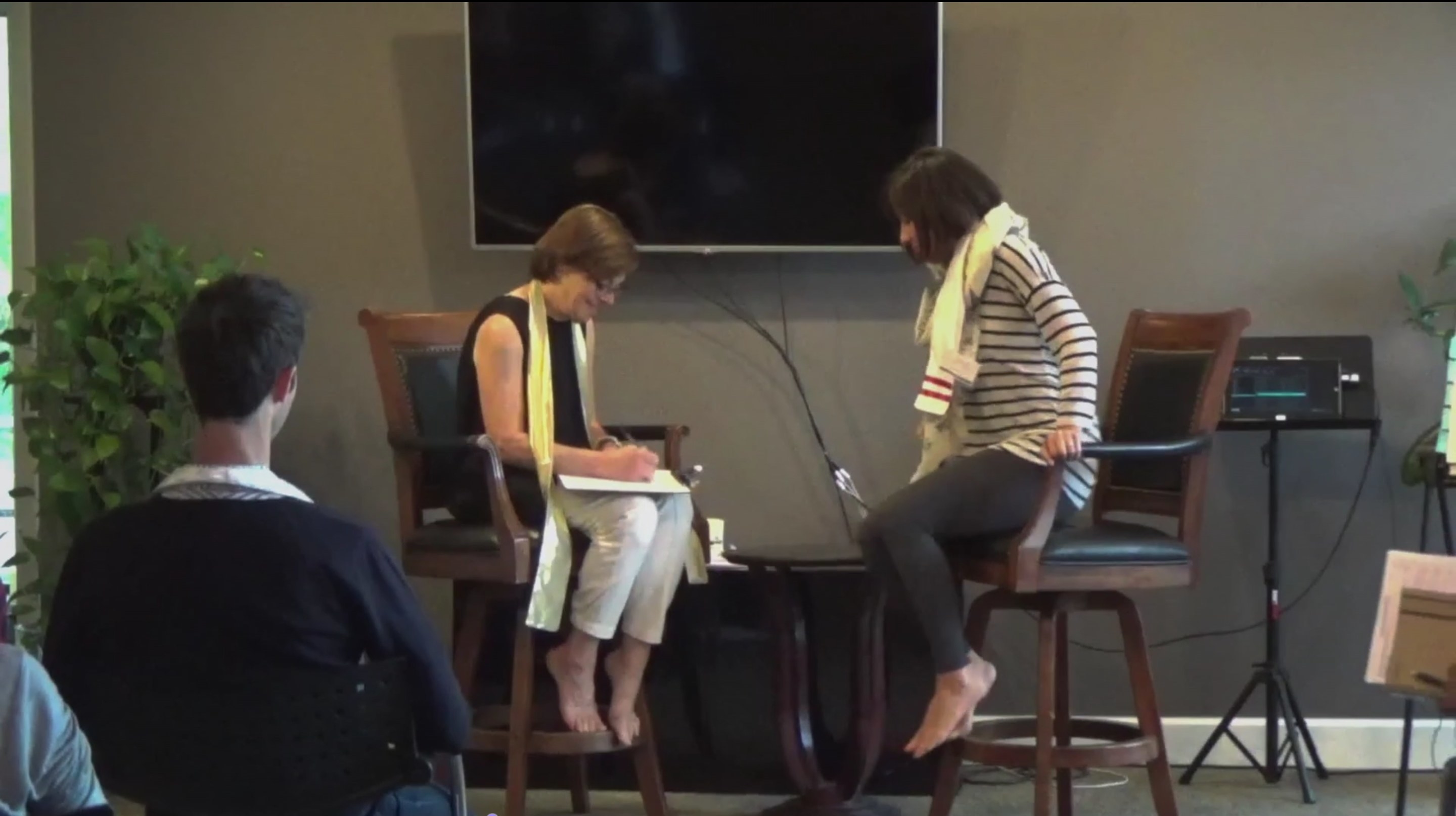 Two barefoot women sitting in front of an audience