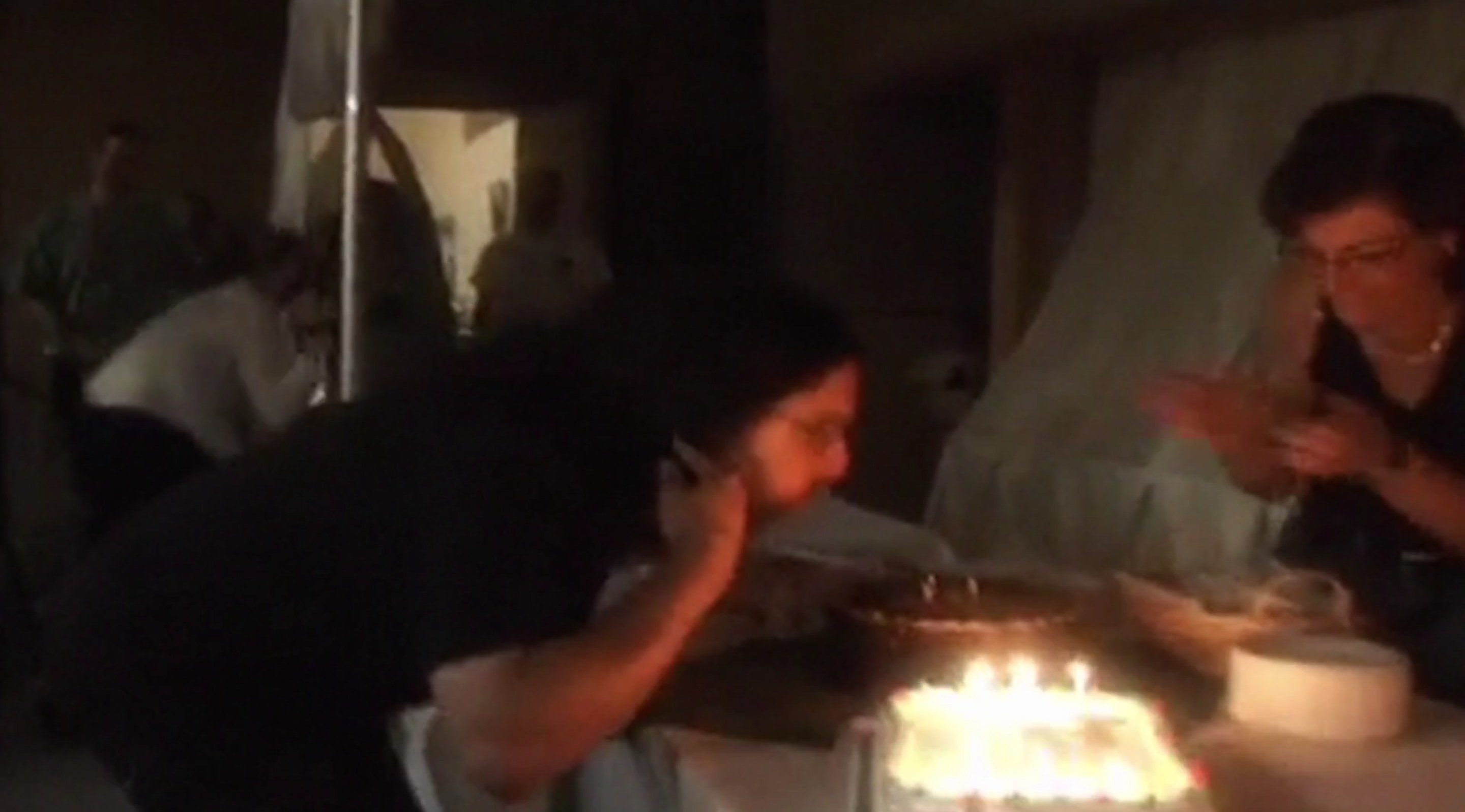 A man and a woman blowing out candles on several cakes