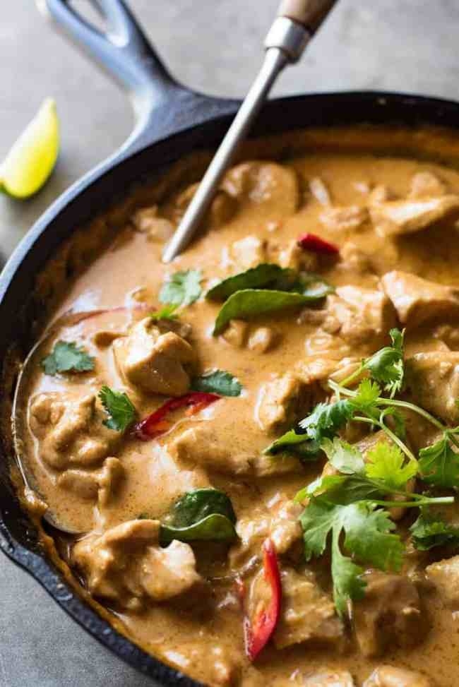 A skillet of coconut mango curry chicken with fresh herbs and hot chilis.