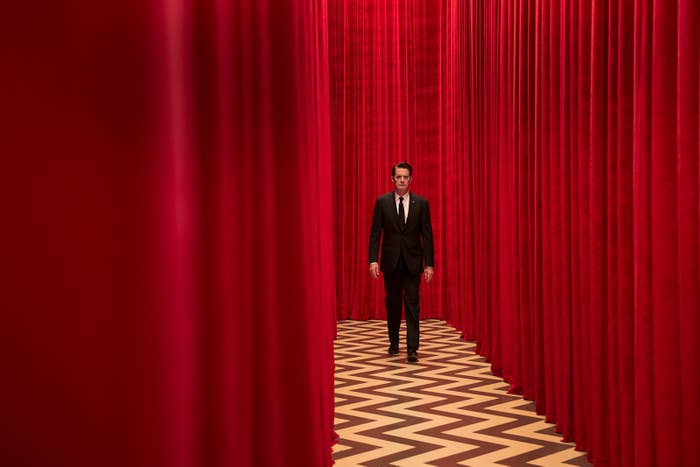 a man in a suit walks down a hallway that is lined with curtains
