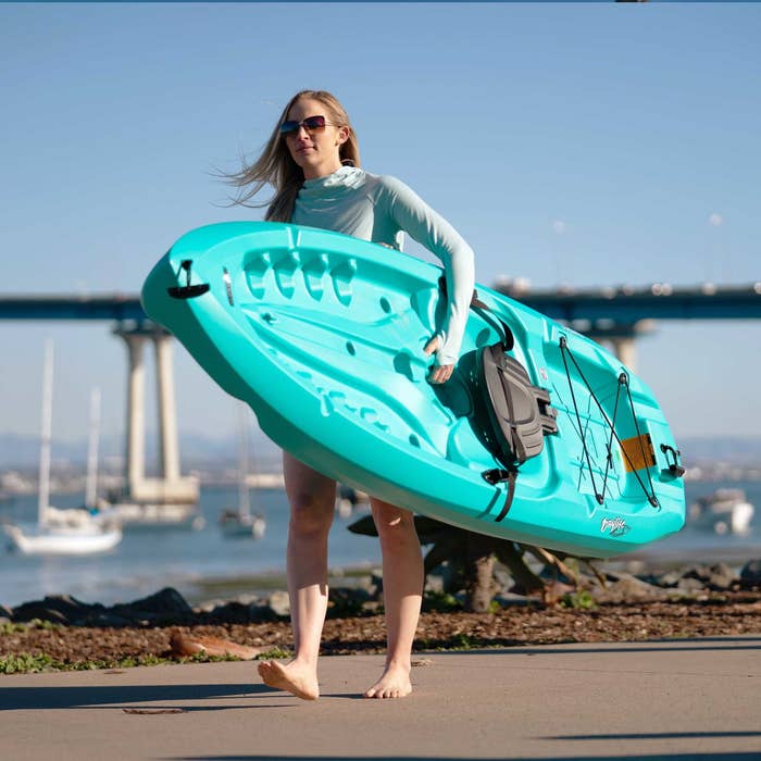 A model carrying a blue kayak in front of the ocean