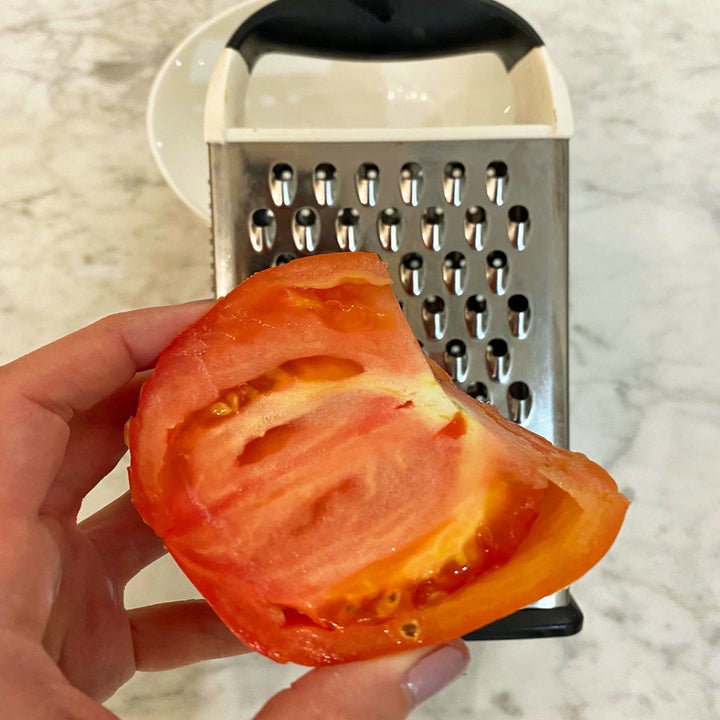 Me holding a halved tomato to a box grater.