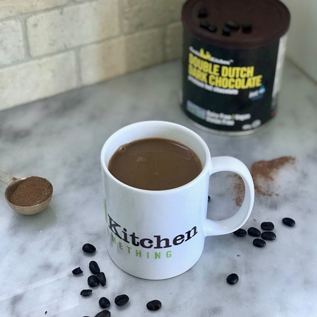 A fresh mug of hot chocolate on a kitchen counter next to some coffee beans and a jar of the cocoa mix