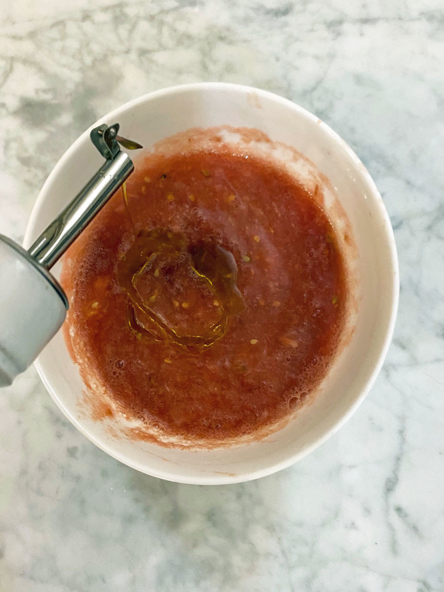 Drizzling olive oil into the garlicky tomato sauce.