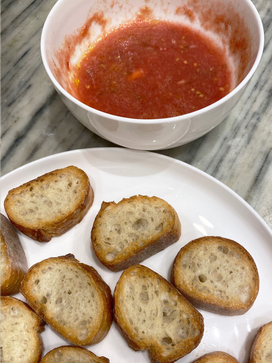 A bowl of tomato sauce and a plate of sliced, toasted bread.