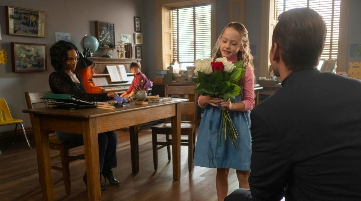 The Haunting of Bly Manor still: Peter Quint gives Flora a bunch of roses as Miss Jessel and Miles look on 