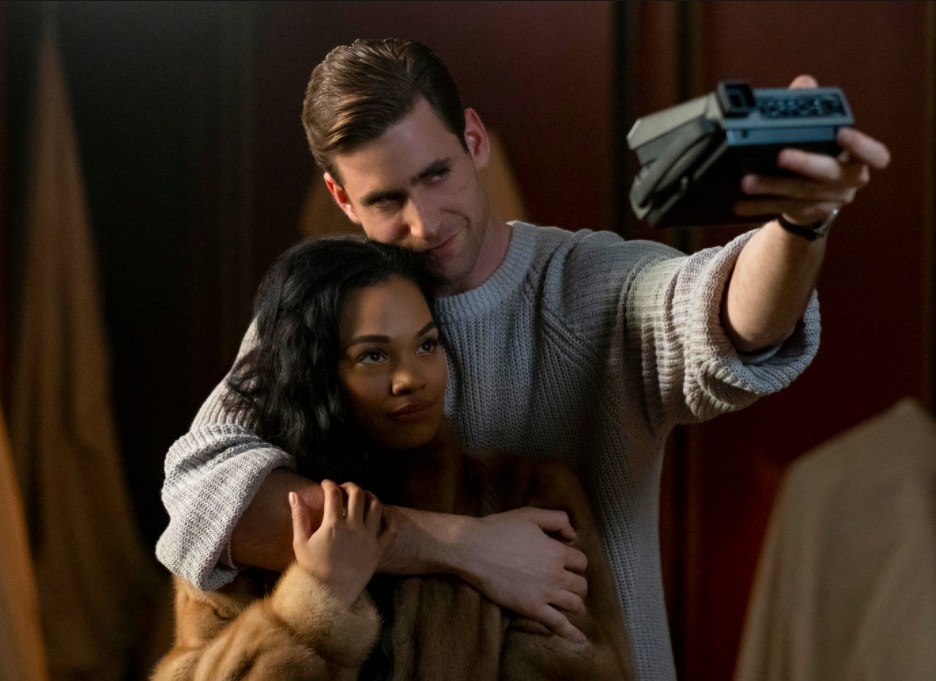 The Haunting of Bly Manor still: Peter Quint wraps one arm around Rebecca Jessel and holds up a polaroid camera focused on them with his other arm