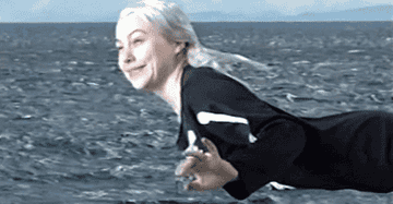 Phoebe Bridgers flying through the sky over an ocean saying &quot;whoo&quot; with a silly smile