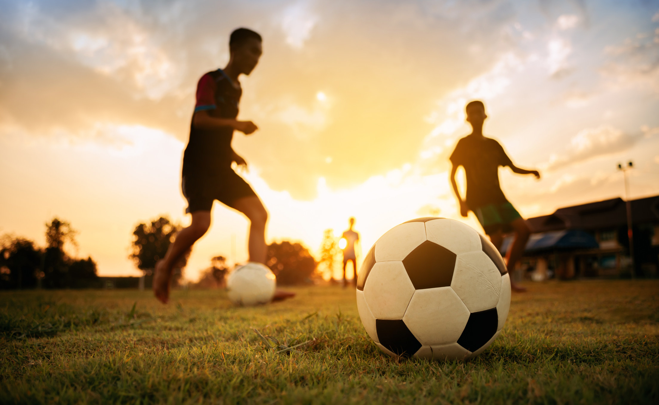 Photo of people playing soccer outdoors, the photo is mostly out of focus except to show the soccer ball laying on the grass