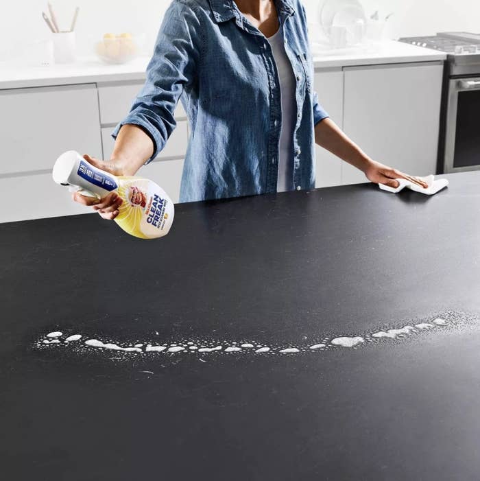 A woman cleaning a black countertop with liquid