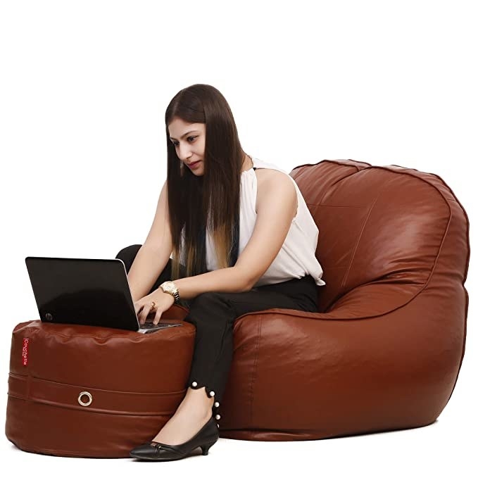 Woman sitting on the bean bag and working on her laptop that’s placed on the footrest.
