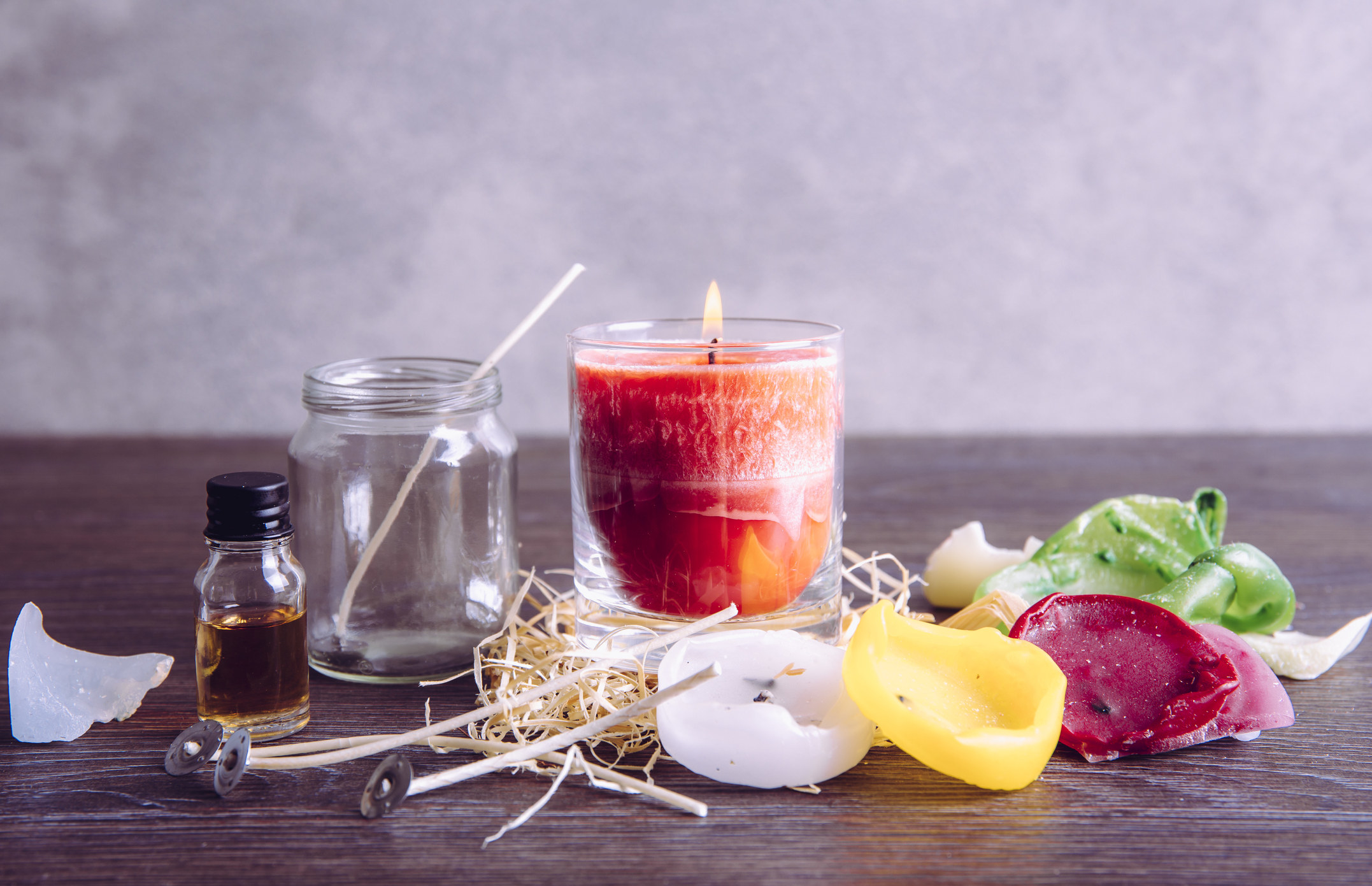 a photo of candles being lit with other waxes on the table, there is oil on the left side and candle waxes in the color green, yellow, red and white on the right side