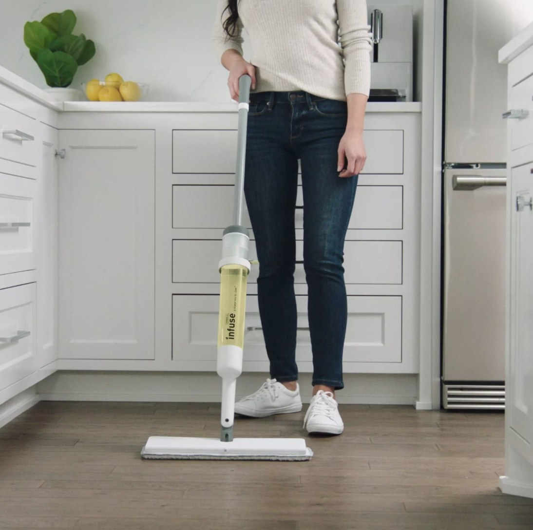 A woman cleaning a hardwood floor with a white wand