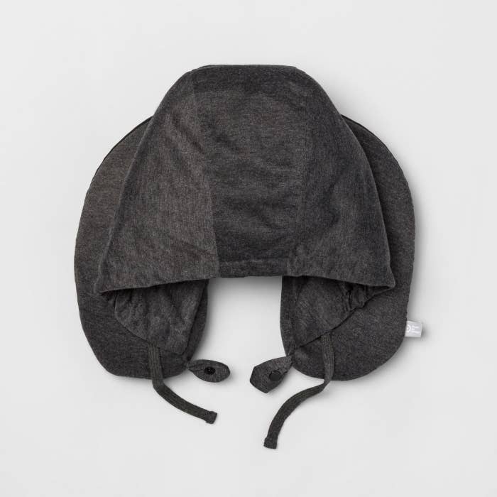 The U-shaped pillow in grey, with a hood sewn to the inner rim of the U, and adjustable straps at the bottom to tighten the hood
