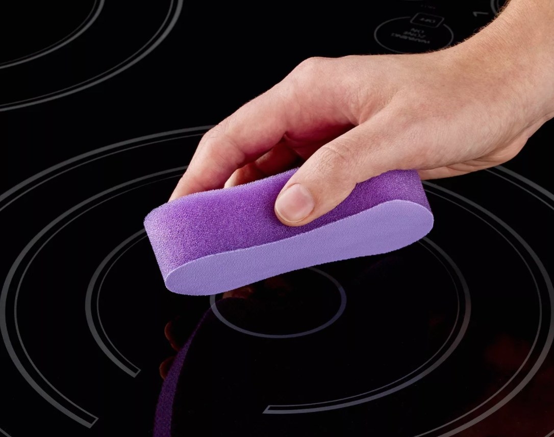 A glass stove with purple sponge cleaning it
