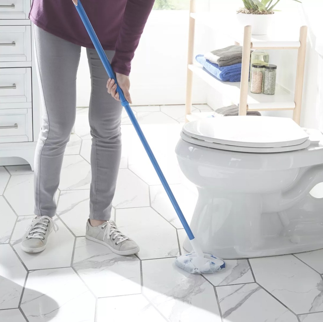 A person cleaning a bathroom floor with a wand