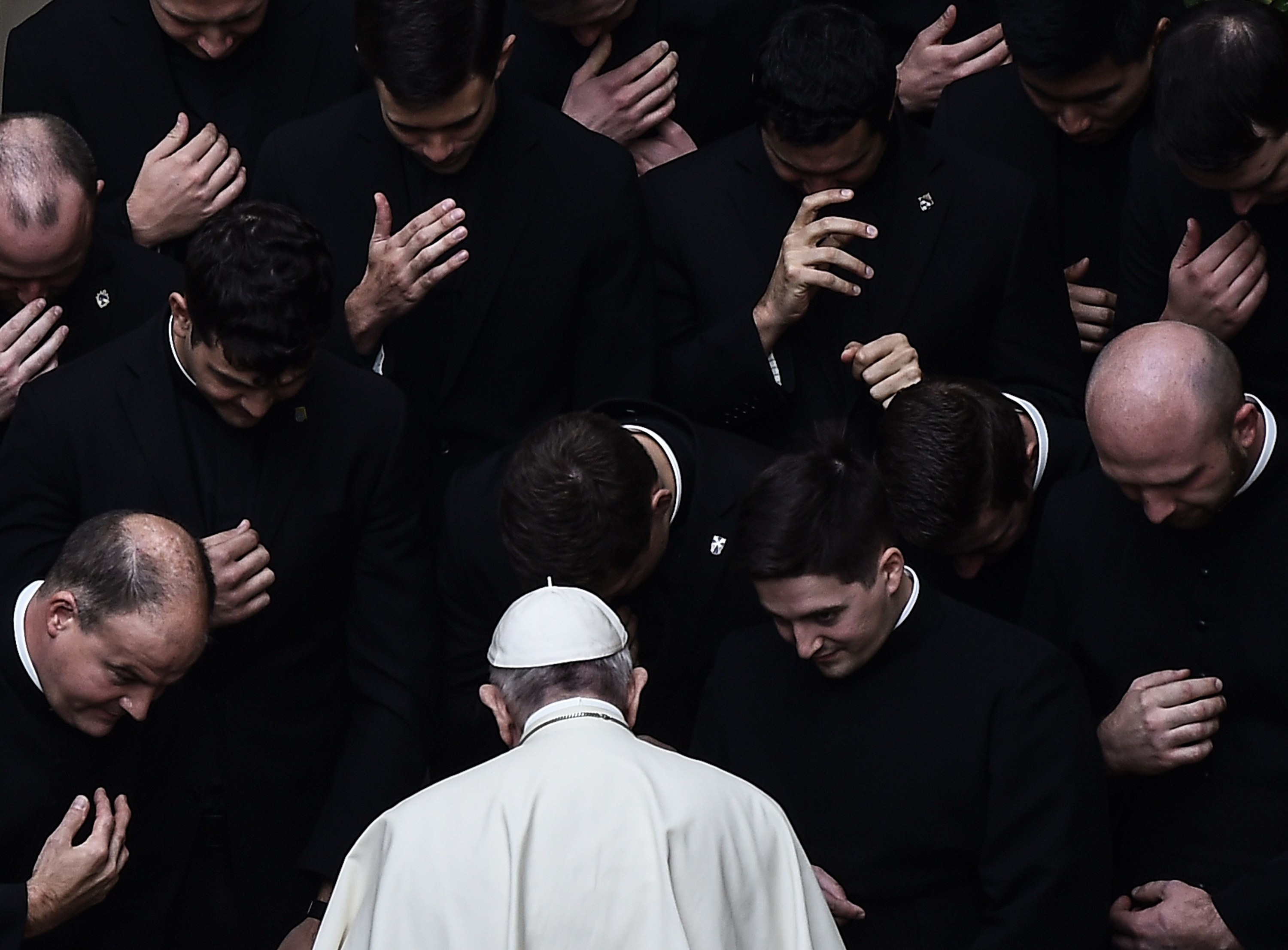The pope, dressed in white, is surrounded by priests, dressed in black