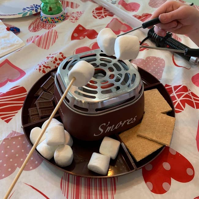A reviewer's s'mores maker in use with marshmallows, chocolate, and graham crackers in the tray