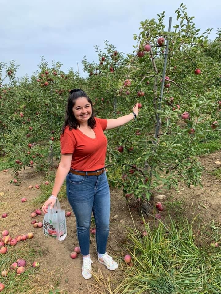 buzzfeed editor apple picking in an orange v-neck tee tucked into jeans