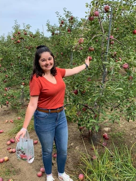 buzzfeed editor apple picking in an orange v-neck tee tucked into jeans