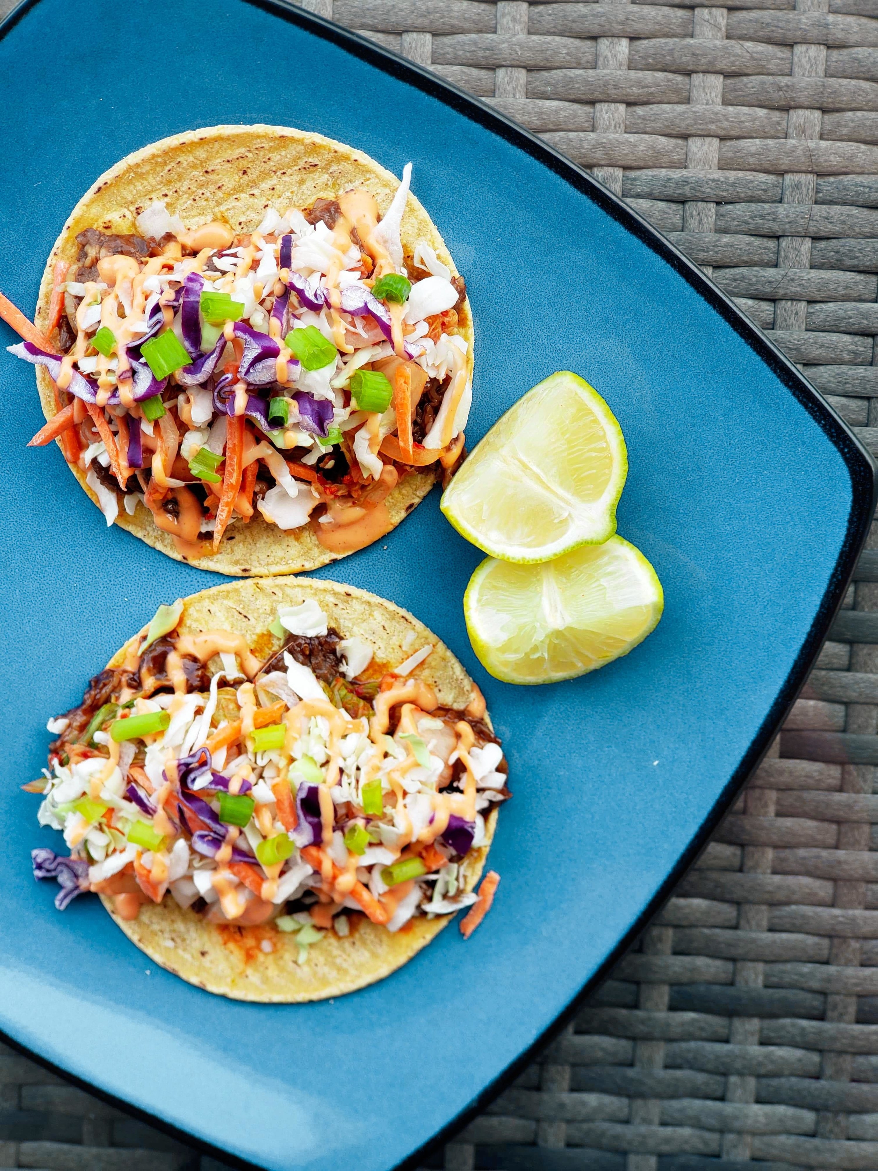 A plate showing two Korean tacos with two lime wedges 