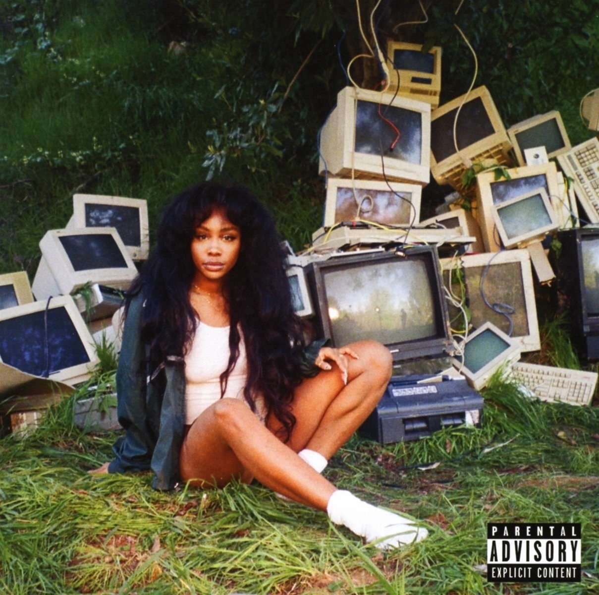 SZA sitting in the grass surrounded by a slew of broken computers. 