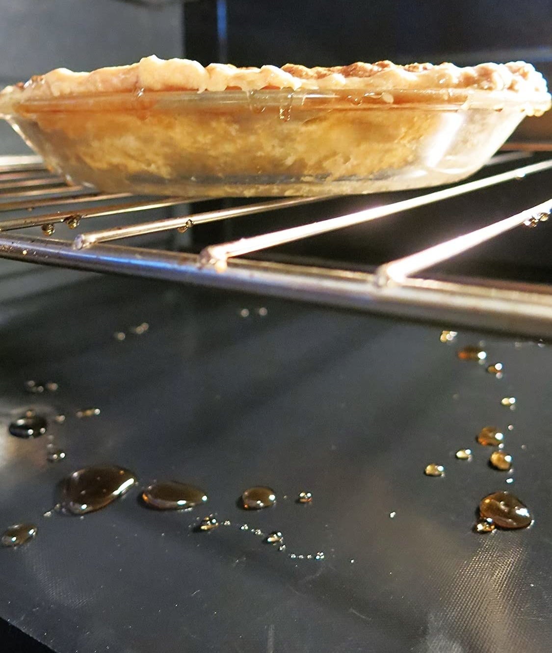 oven liner in bottom of oven catching drippings from a baking pie 