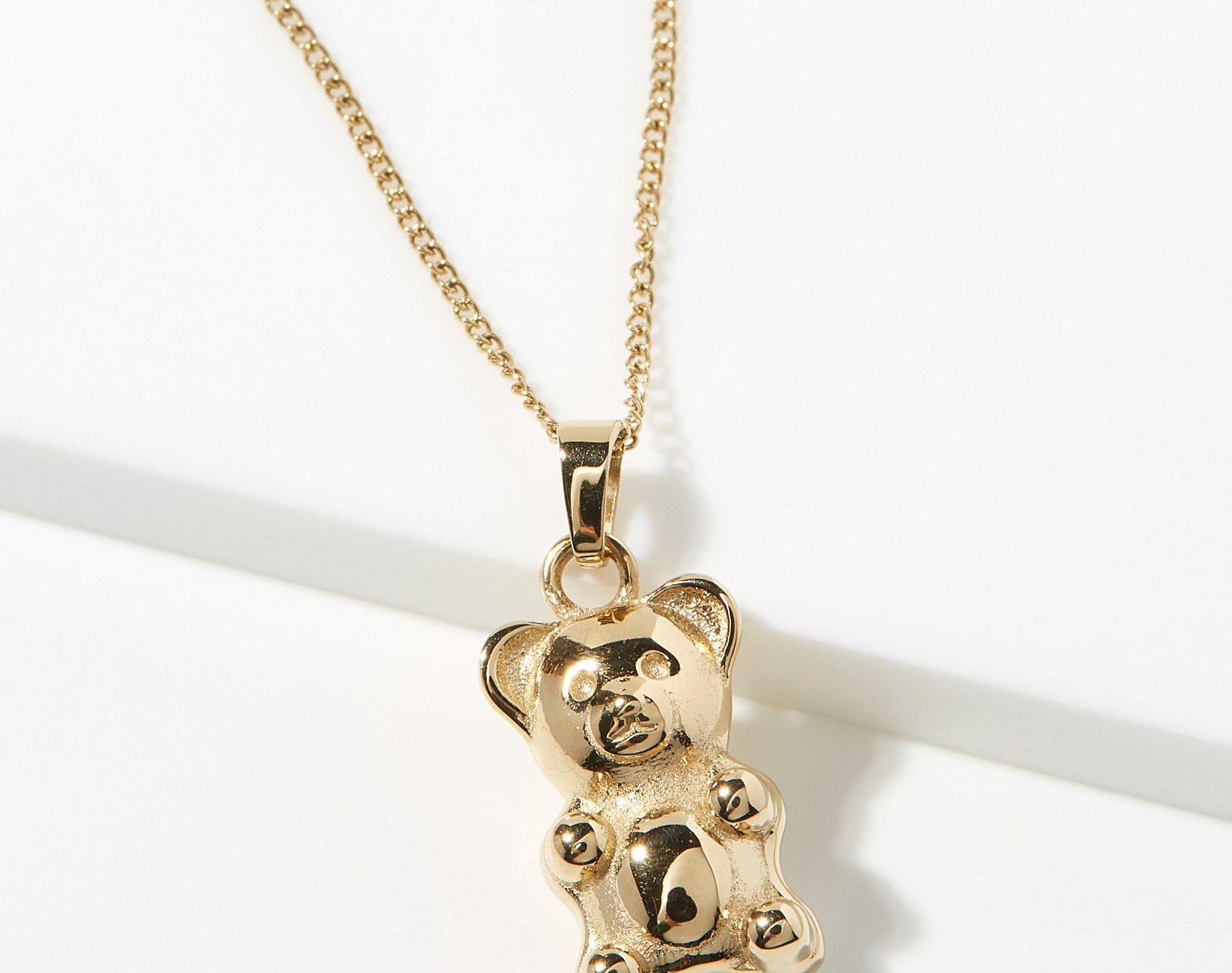 A gold necklace with a gummy bear shaped pendant