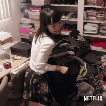GIF of a smiling Marie Kondo lugging a bag full of old clothing. 