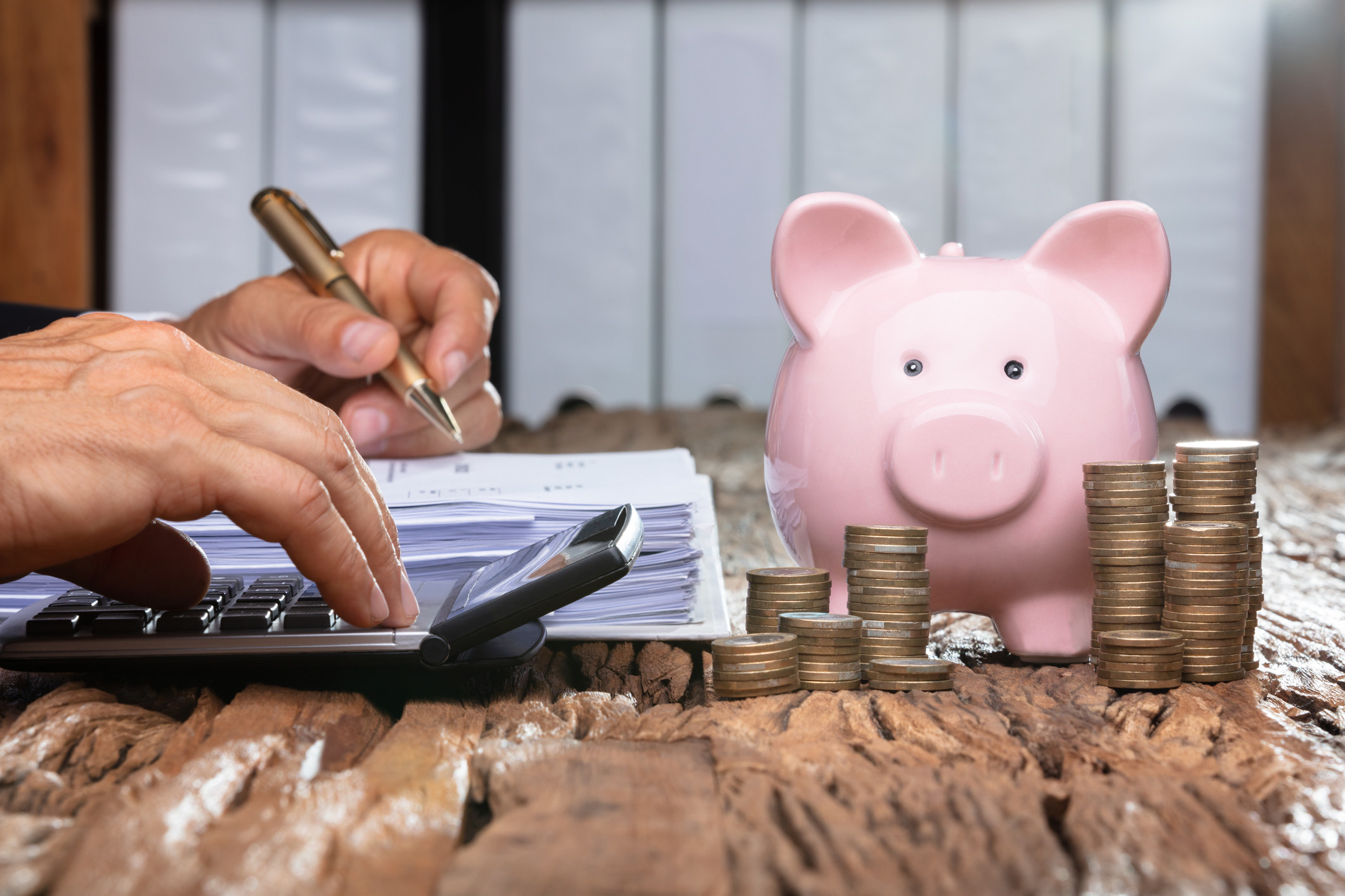 A person creating a budget with a calculator and piggy bank