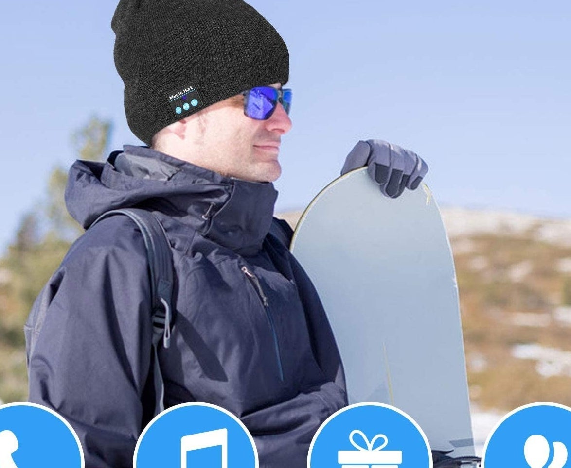 A smiling person wears the toque while preparing to snowboard