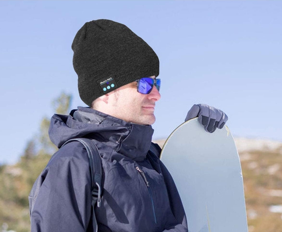 A smiling person wears the toque while preparing to snowboard