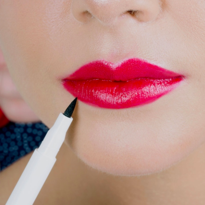 A close up of a person using the pen to touch up their lipstick