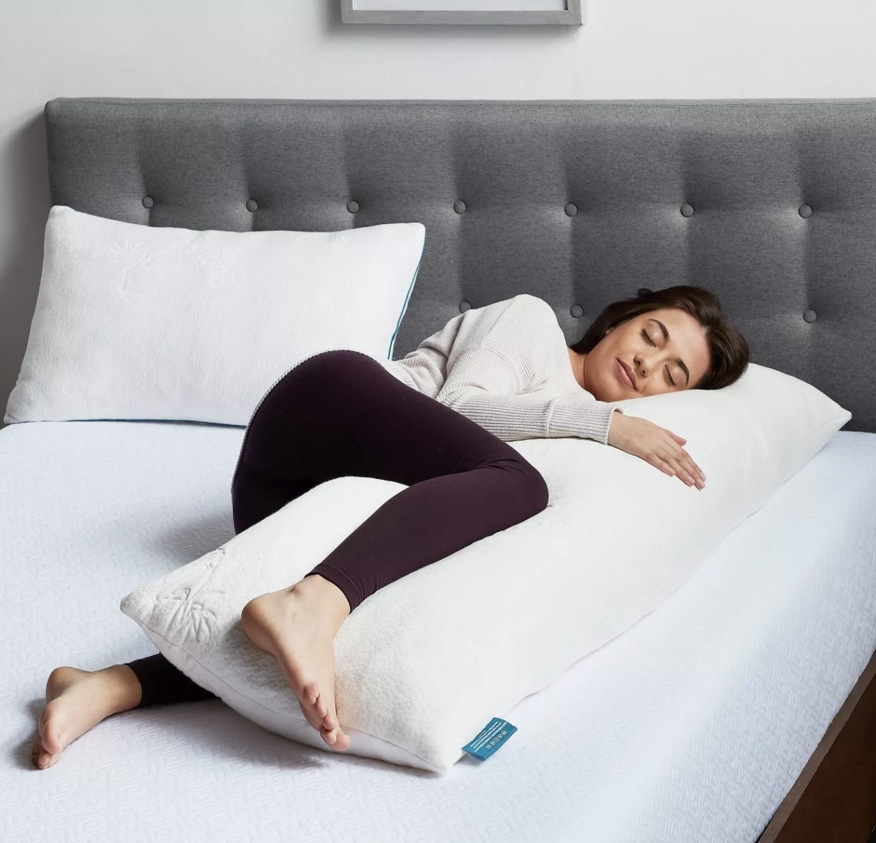 a model cuddling a memory foam body pillow while laying in bed