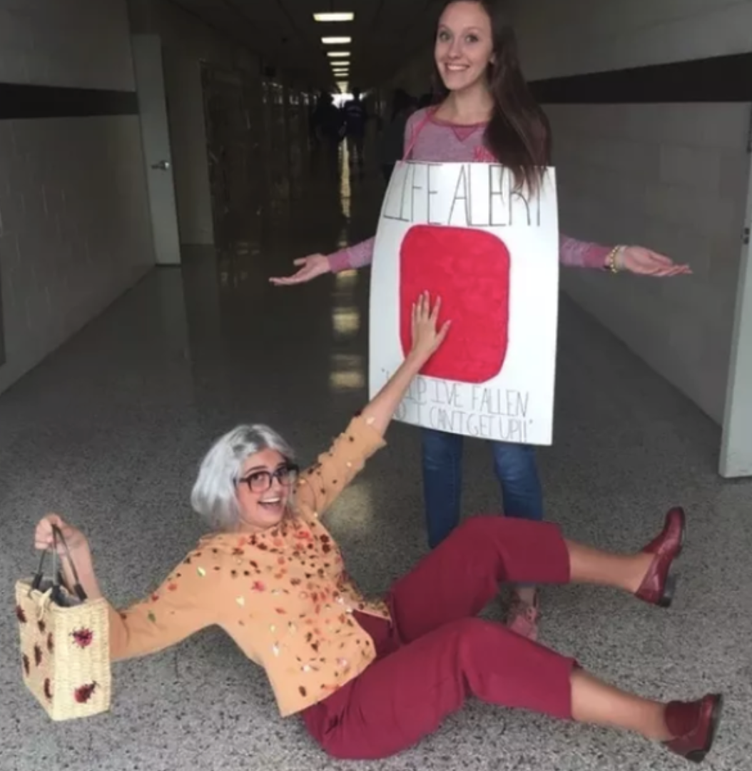 Someone dressed as an old lady, laying on the ground, pressing someone who used poster board to dress up like a Life Alert button