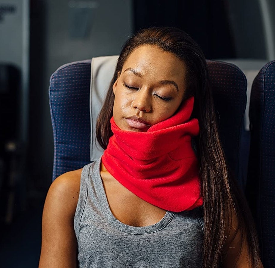 A person sleeping on a bus while wearing the fleecy pillow around their neck