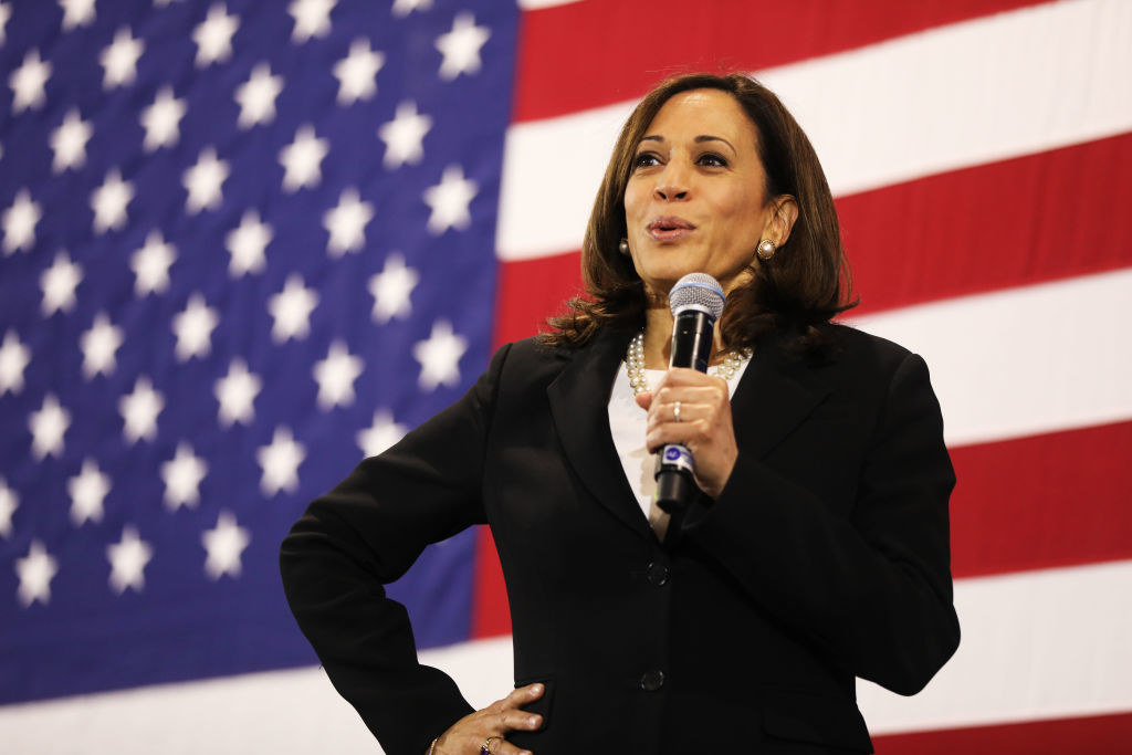 Kamala Harris holding a mic in front of an American flag