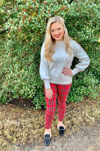 A reviewer wearing the white chevron stitch and pom pom sweater in white with plaid pants
