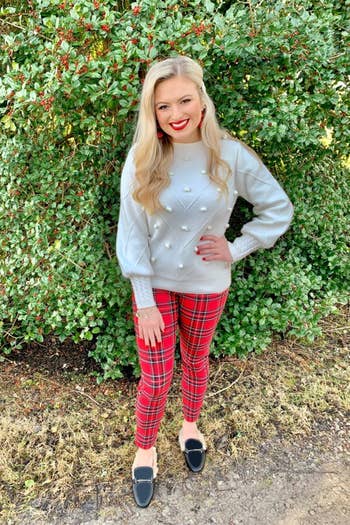 A reviewer wearing the white chevron stitch and pom pom sweater in white with plaid pants