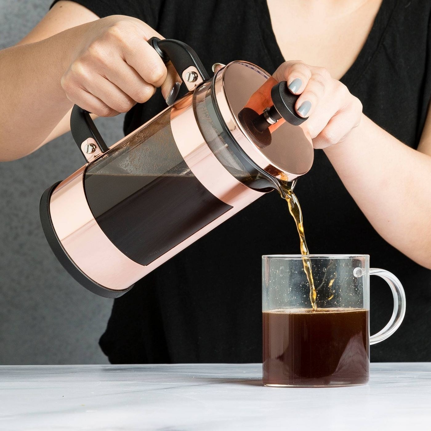 A model pours coffee from the copper french press into a glass mug