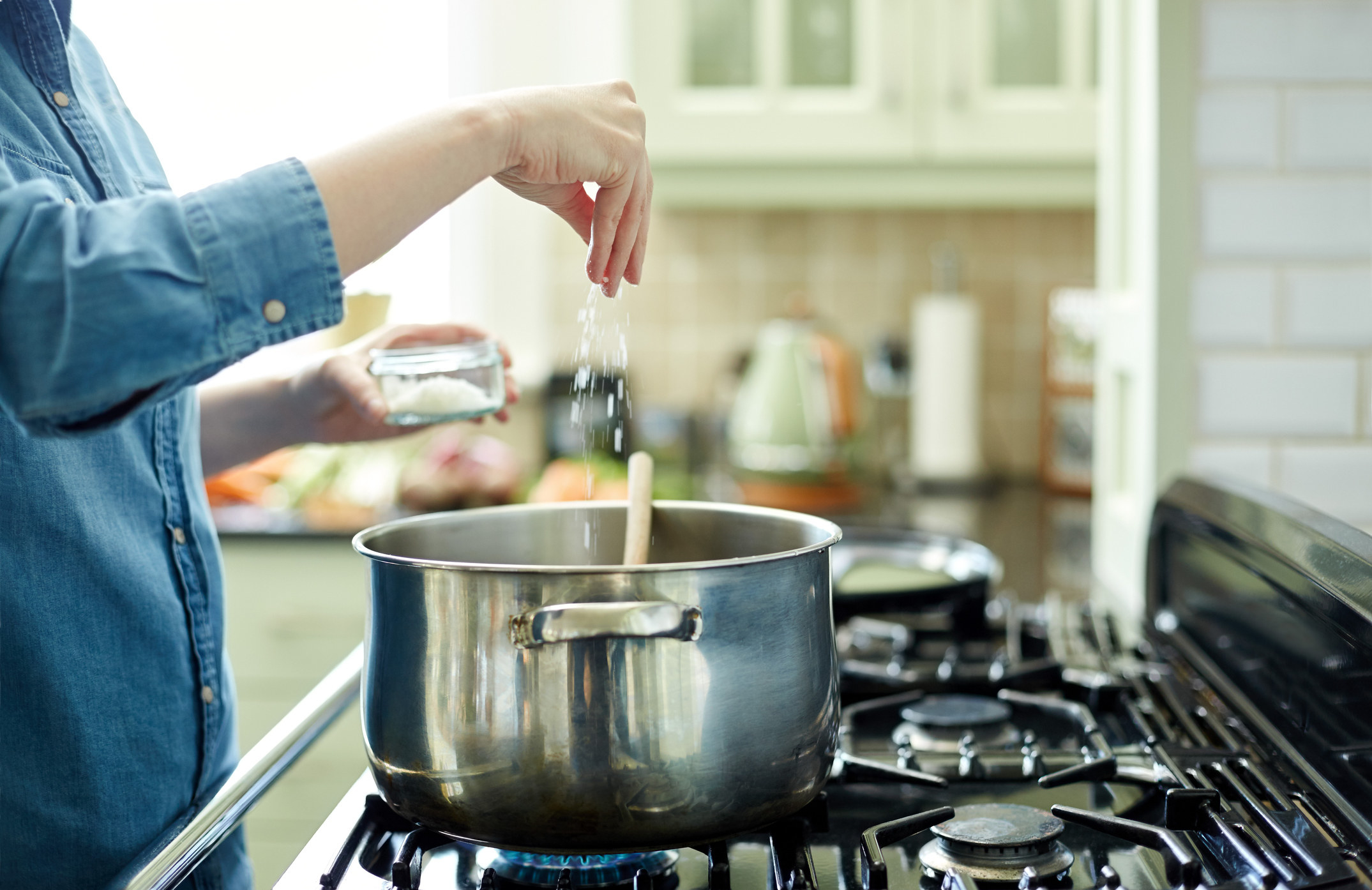 A person adding salt to a pot on the stove