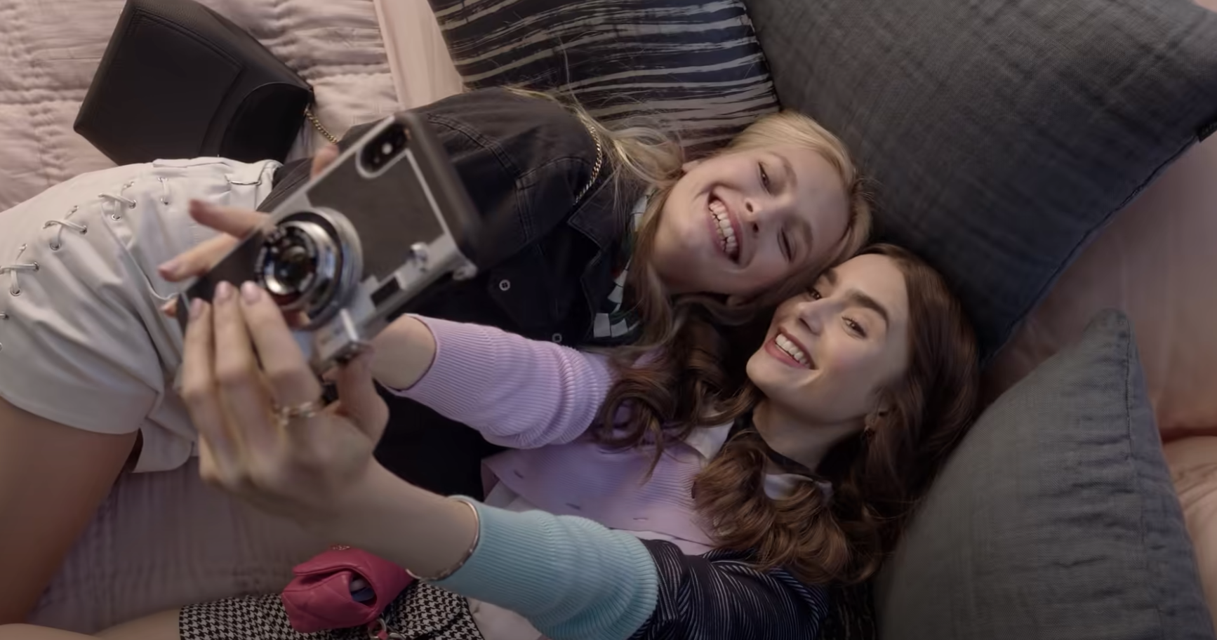 Emily and Camille smiling for the camera in a bed in &quot;Emily in Paris&quot;