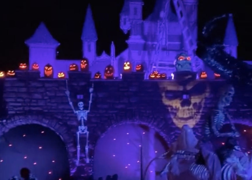 A castle illuminated with purple lights at night featuring skeletons and jack-o-lanterns