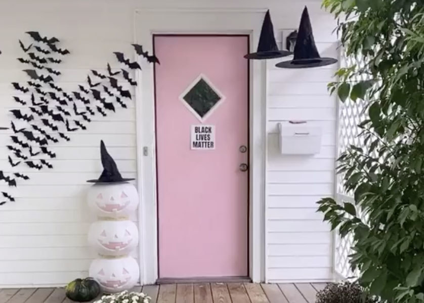 A home with a pink door with white and pink pumpkins outside and bat decorations