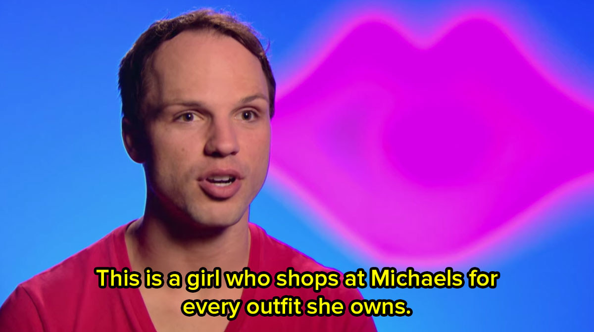 A close up of a contestant from Drag Race in front of a bright blue background giving a talking head interview and saying this is a girl who shops at Michaels for every outfit she owns