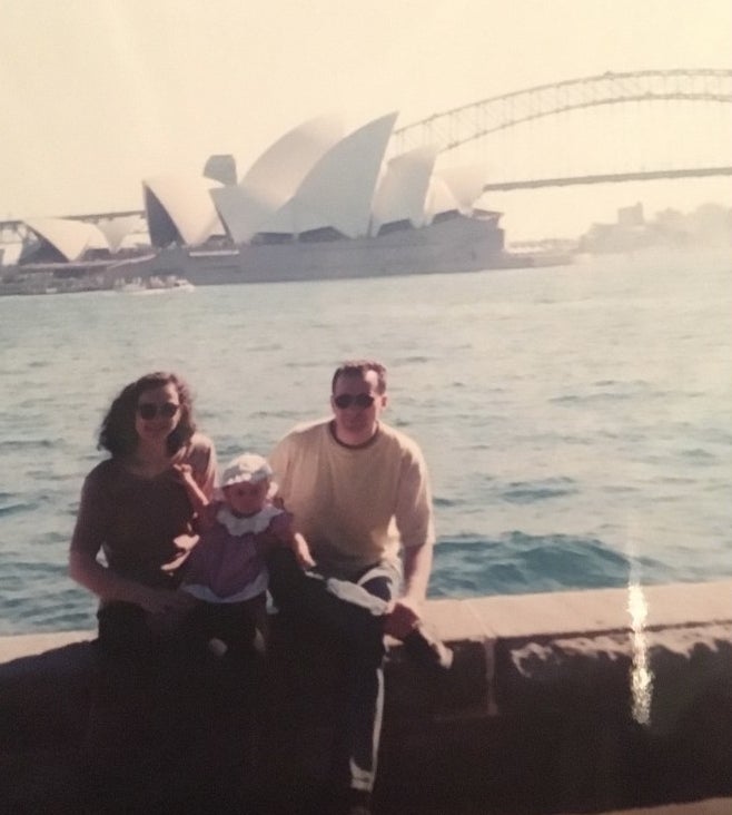A young family with a baby posing in front of the Opera House and Sydney Harbour Bridge