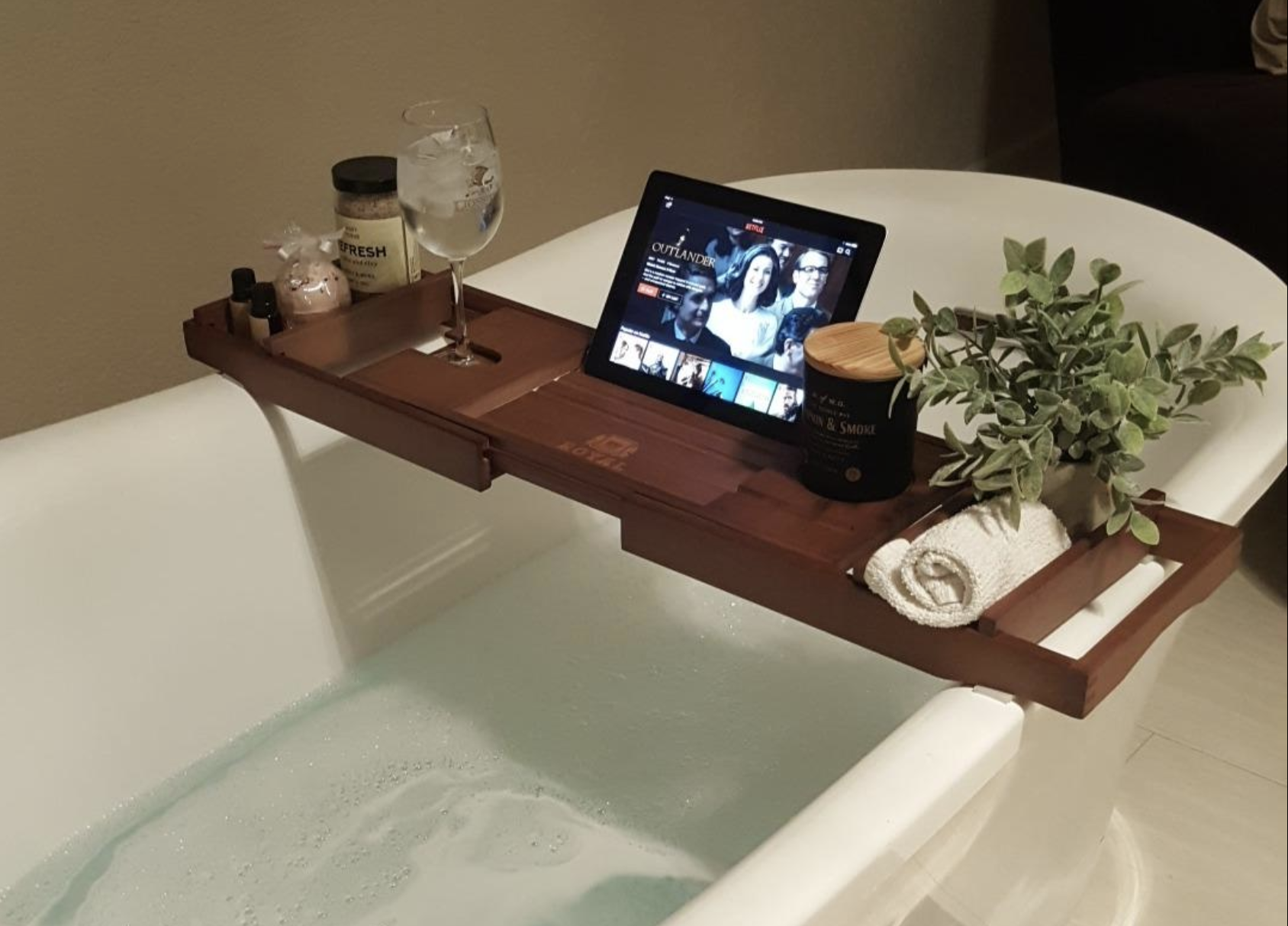 Reviewer image of a wooden bath caddy holding an iPad, washcoth, plant, candle, wine glass, bath salts 