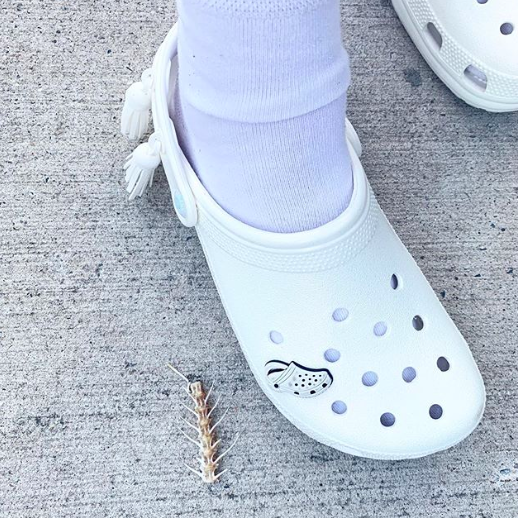 A white pair of Crocs with a white Crocs jewel inside one of the holes 