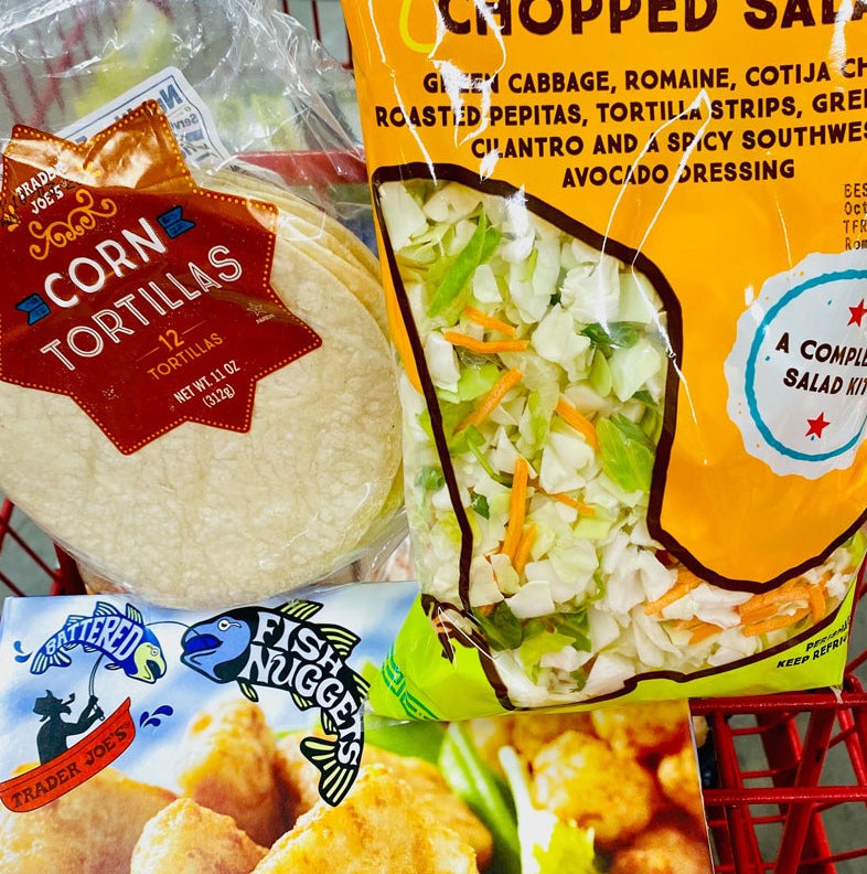 A box of Trader Joe&#x27;s battered fish nuggets with a bag of slaw and tortillas in a cart.