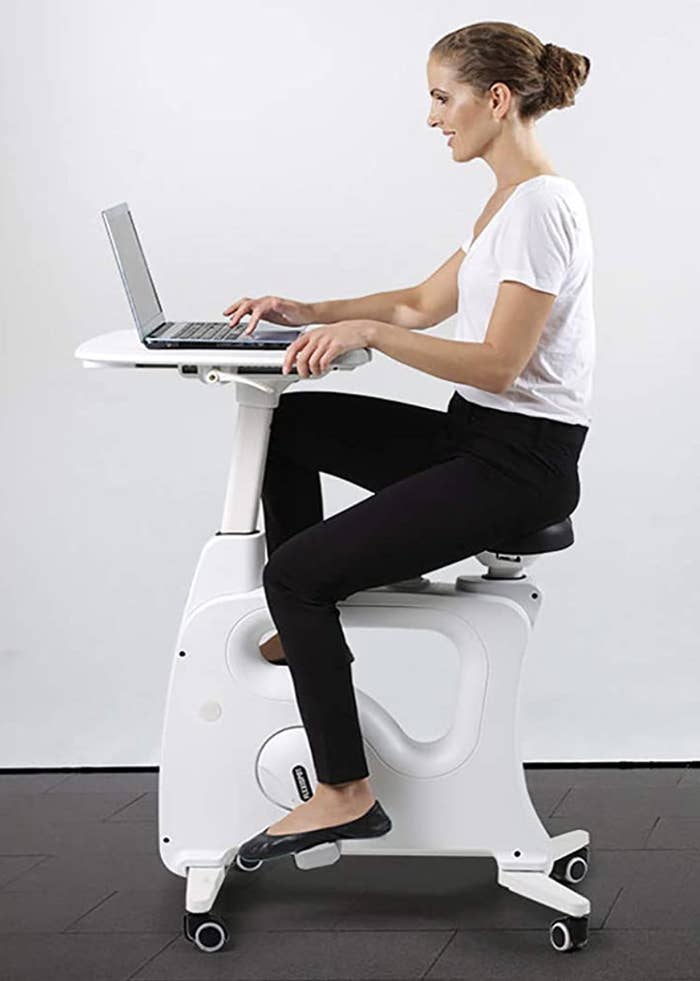 A model on a white bike desk with a tray steadying their laptop 